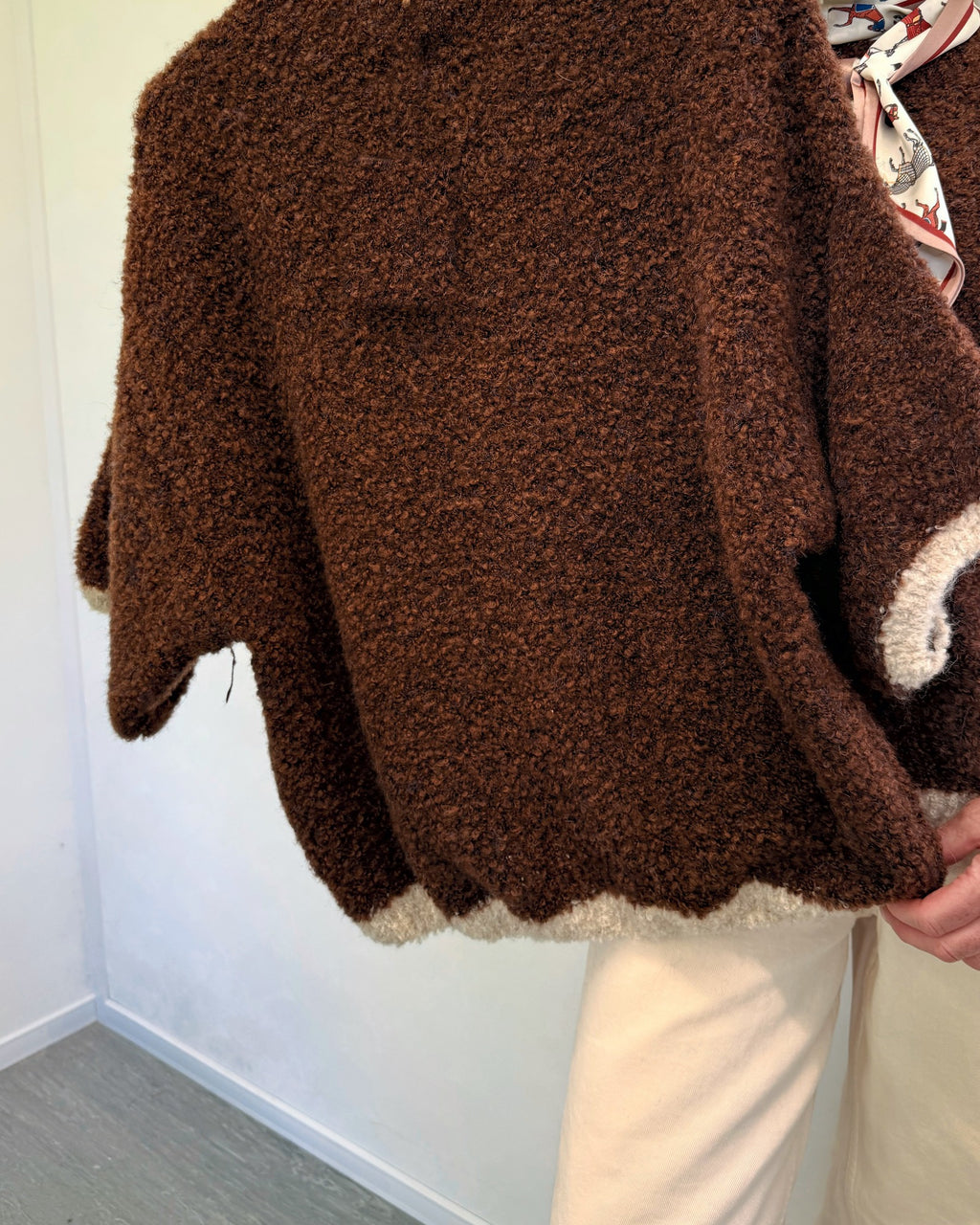 Brown and cream bouclé soft textured knit jumper held up on a hanger showing the cream bouclé trim at the cuffs and hem