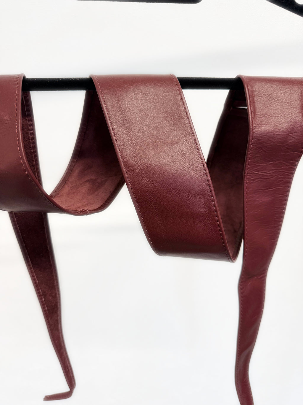 Burgundy real leather obi sash belt draped over a hanger, close-up