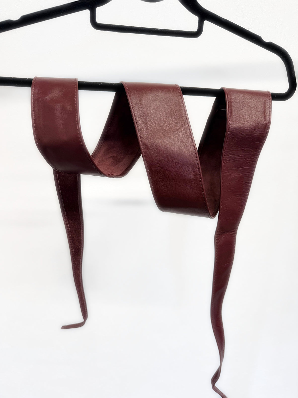Full length of the burgundy leather obi sash belt on a hanger