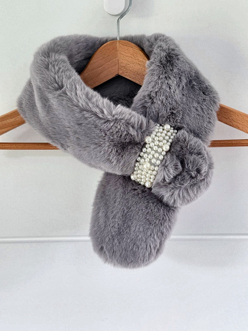 Grey luxe faux fur neck warmer with pearl loop brooch on a hanger