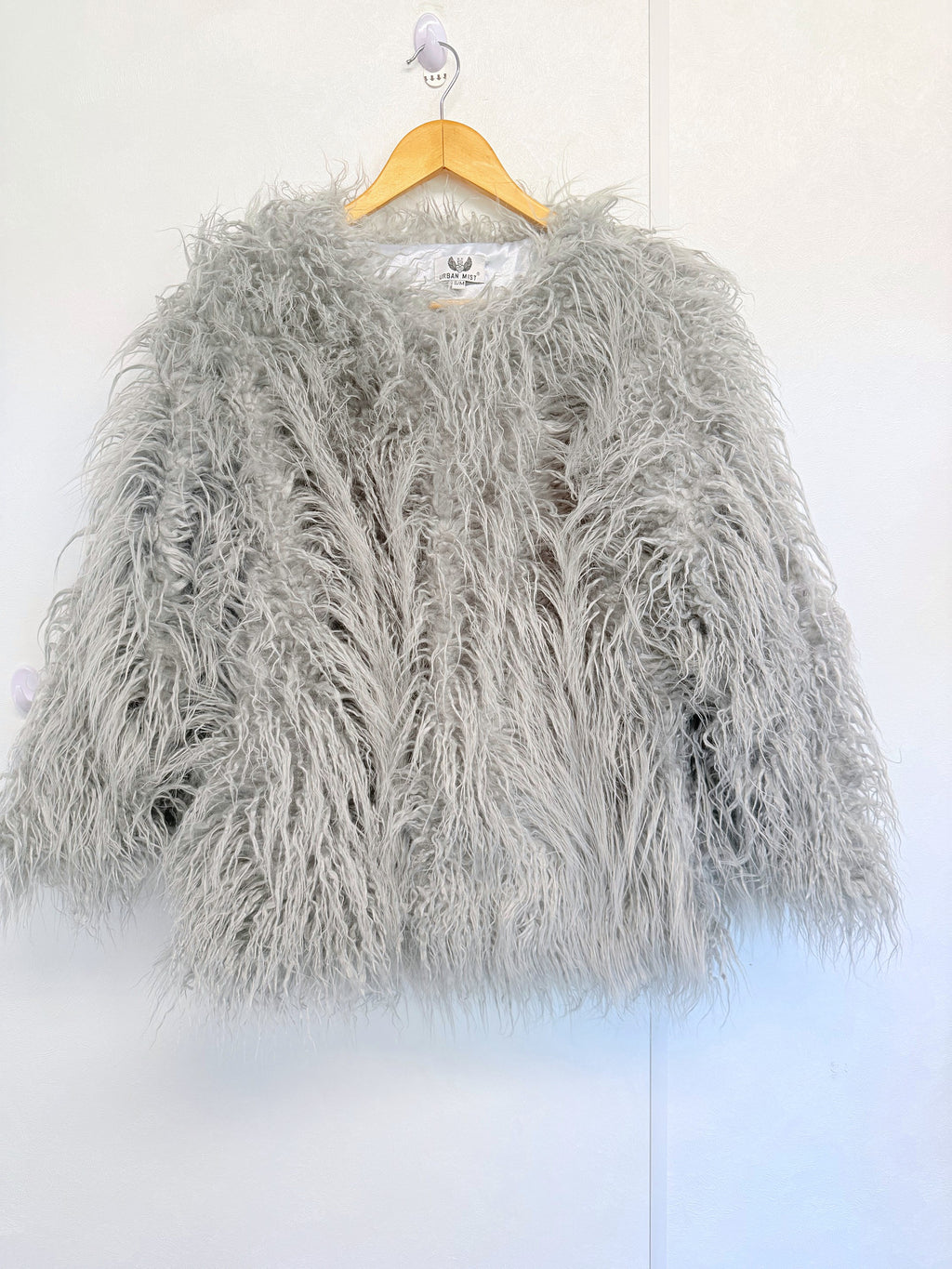 Light grey Mongolian faux fur coat on a hanger showing the fluffy texture